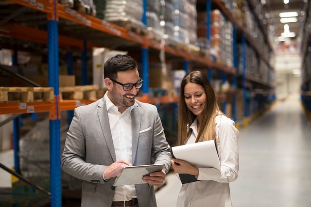 Warehouse manager reviewing inventory list with a pallet of plumbing and lighting supplies in the background (plg supplies)